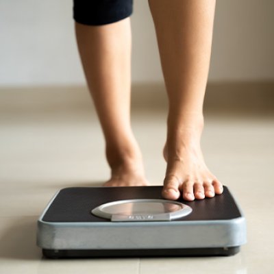 A woman's lower legs stepping onto weighing scales.